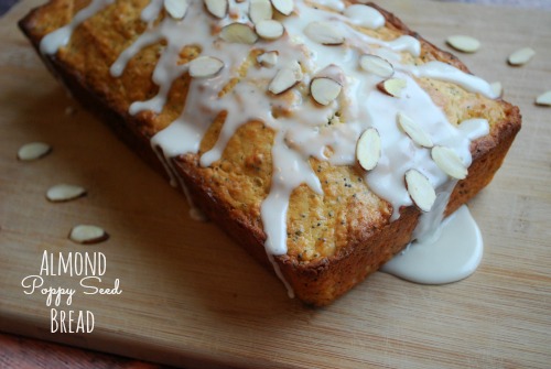 loaf of almond poppy seed bread on wood cutting board with icing drizzle and almond slices