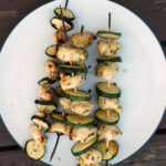 a plate with skewers of chicken and zucchini on it