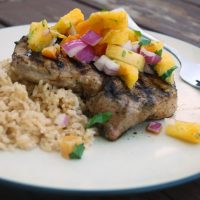 grilled pork chop on white plate, topped with pineapple salsa