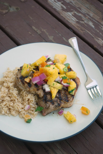 A plate of food on a table, with Pineapple salsa on grilled Pork chop with brown rice