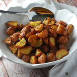 A white bowl on a wooden table with dijon roasted red potatoes