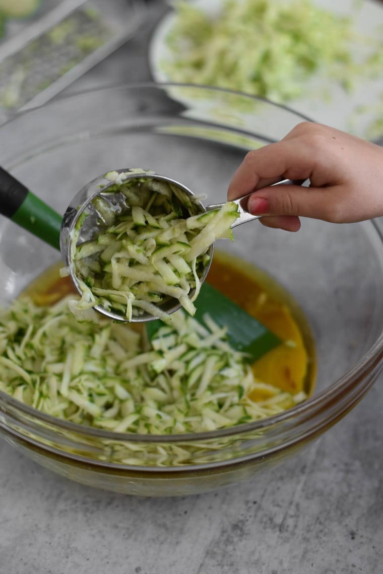 kid hand adding shredded zucchini into bowl