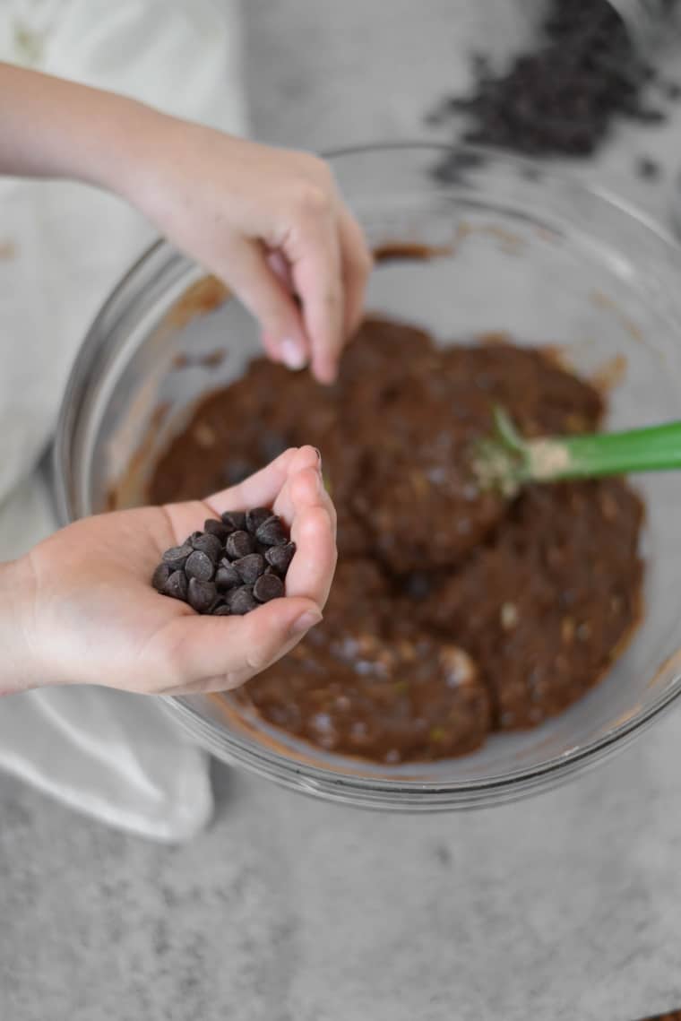 kid hand placing chocolate chips into zucchini brownie batter