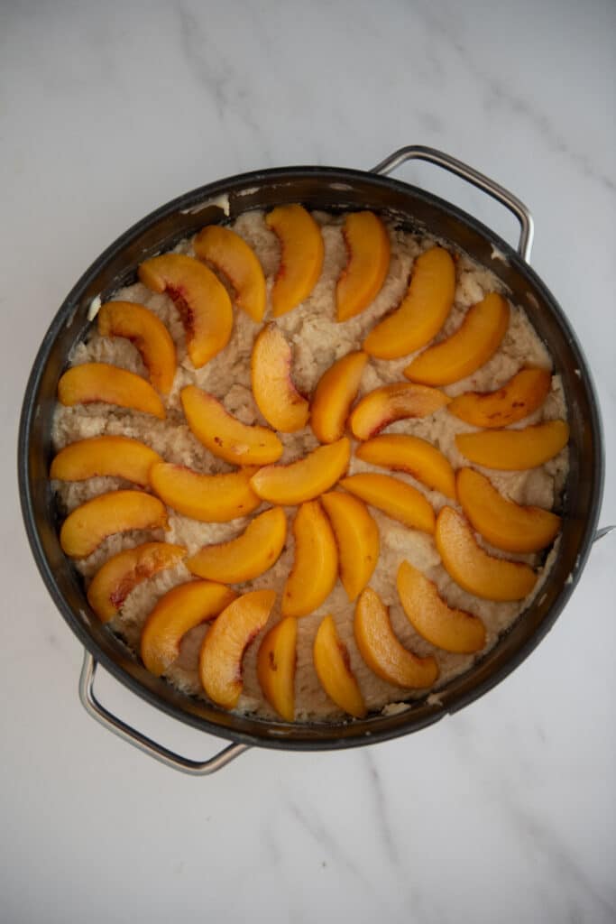 overhead of springform pan with batter and sliced peaches arranged