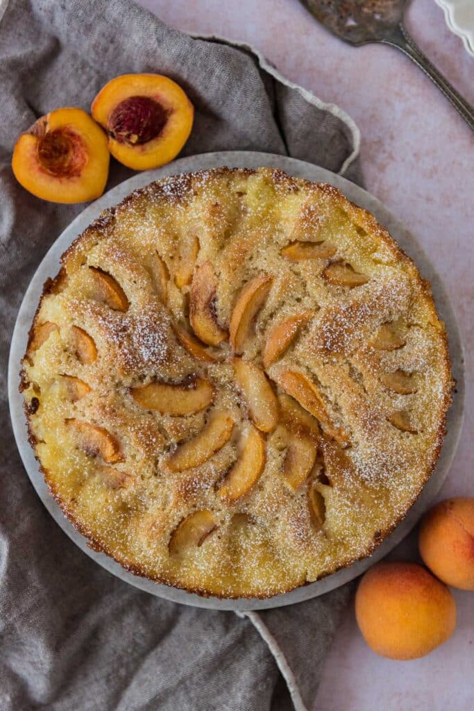overhead of peach kuchen on marble cutting board with peaches around
