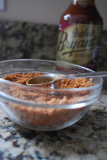 small glass bowl with homemade pork rub and measuring spoon, with bbq sauce bottle in background