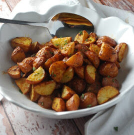 A white bowl with dijon roasted red potatoes and a silver spoon