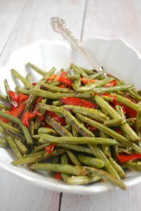 A white bowl with green beans and roasted red peppers