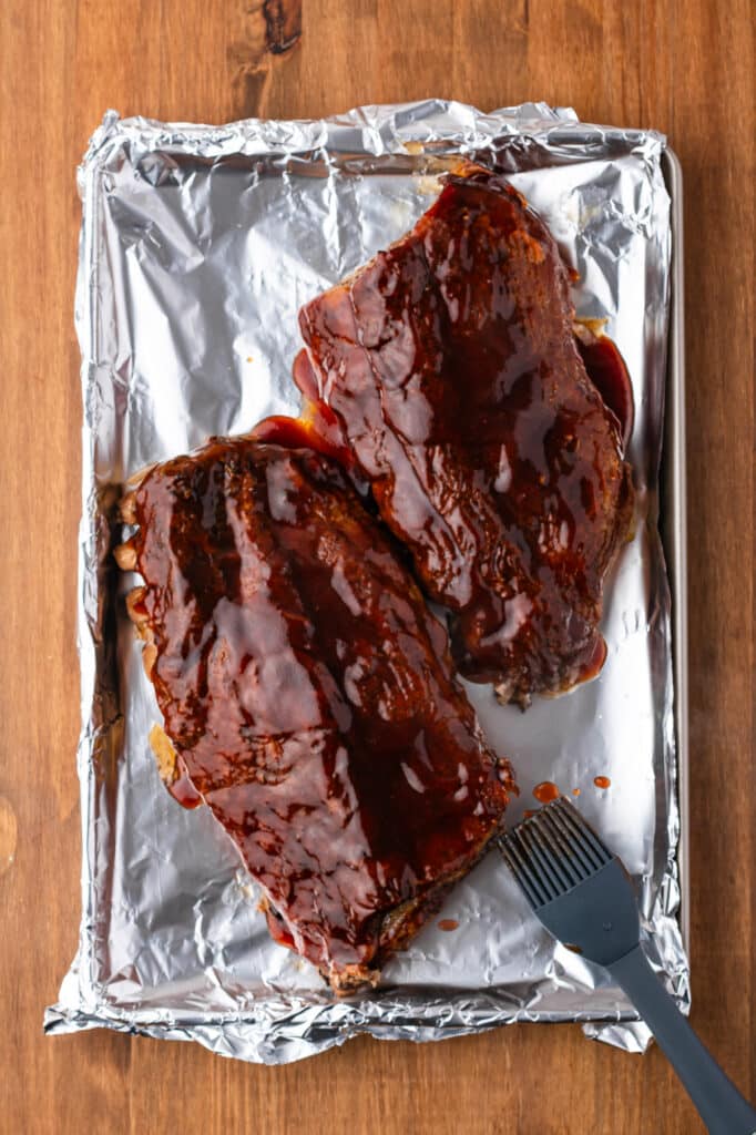 baby back ribs smeared in barbecue sauce on baking tray lined with foil