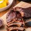 slow cooker baby back ribs on wooden cutting board with slow cooker and dish of corn in background