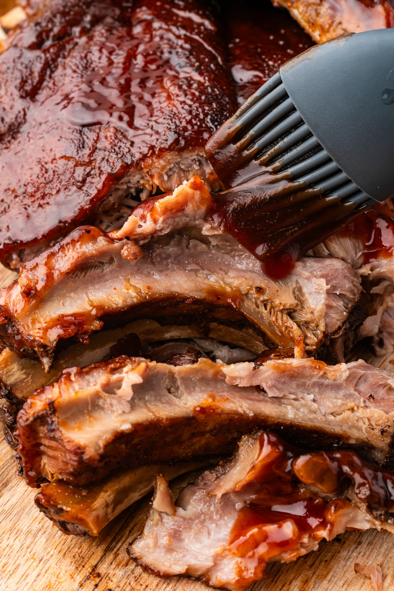 slow cooker baby back ribs on cutting board with black silicone pastry brush smothering bbq sauce over top
