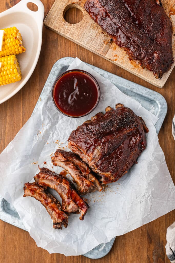 baby back ribs on tray with barbecue sauce next to more ribs and dish of corn