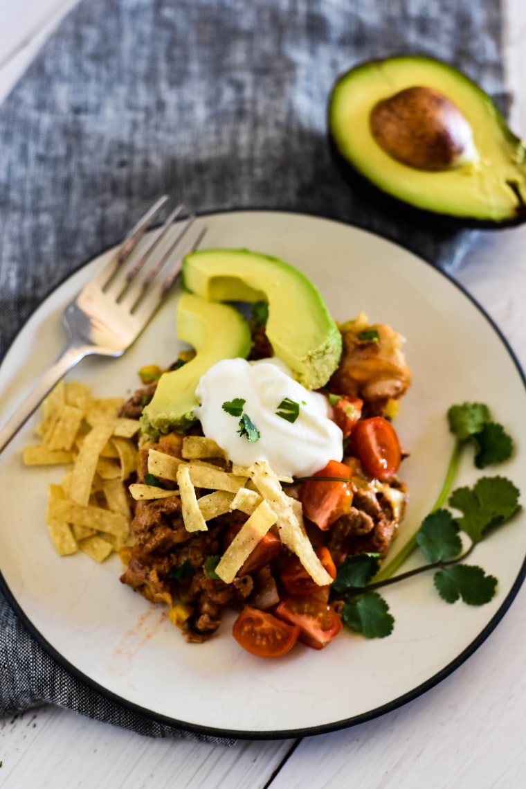 plate of enchilada casserole with avocado, sour cream, and tomatoes