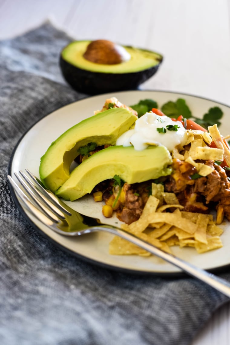 plate of beef enchilada casserole with avocado slices, chips and sour cream
