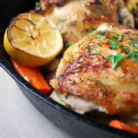 close up of roasted chicken thigh with carrots and lemon slices