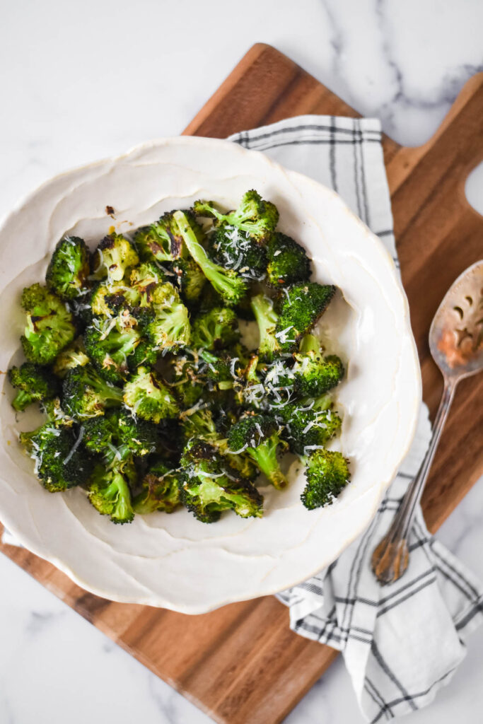roasted broccoli in white bowl with napkin and wooden tray underneath bowl