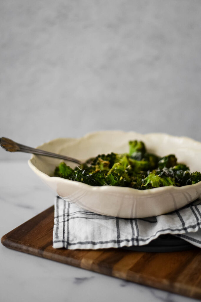 side view of broccoli in white bowl with serving spoon