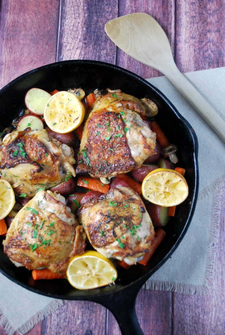 cast iron skillet with chicken thighs, potatoes, carrots and lemons