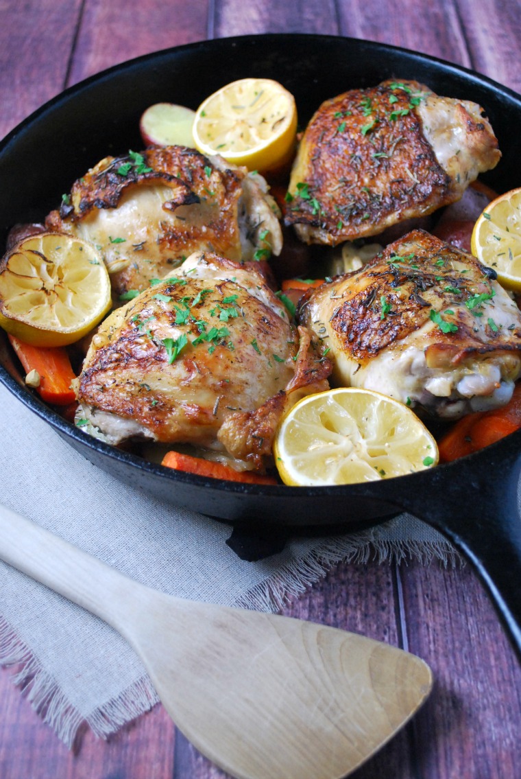 cast iron skillet with chicken, carrots, and lemon