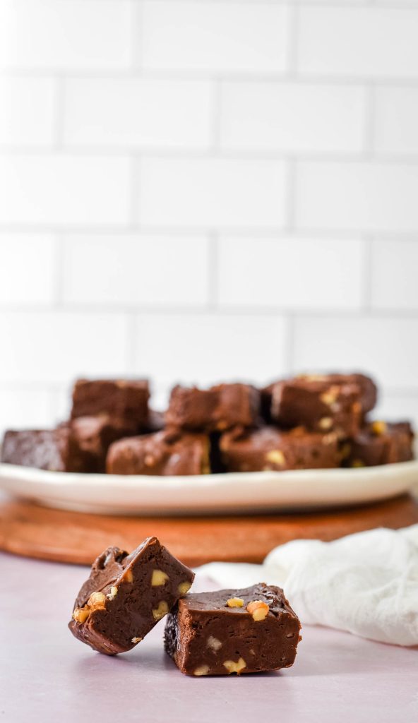 two pieces of chocolate walnut fudge on counter in front of platter