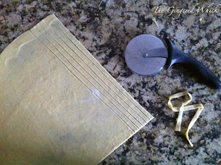 sheet of dough being cut with pizza cutter into pasta strips