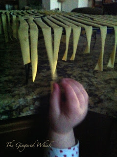 freshly made pasta drying on rack with child\'s hand reaching up to grab a piece 