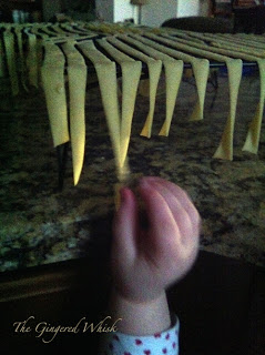 freshly made pasta drying on rack with child's hand reaching up to grab a piece 