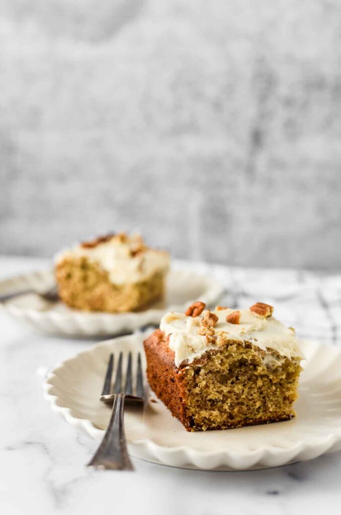 two slices of banana walnut cake on two white plates with forks