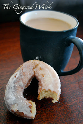 a close up of a sourdough donut with bite taken out of it next to cup of coffee