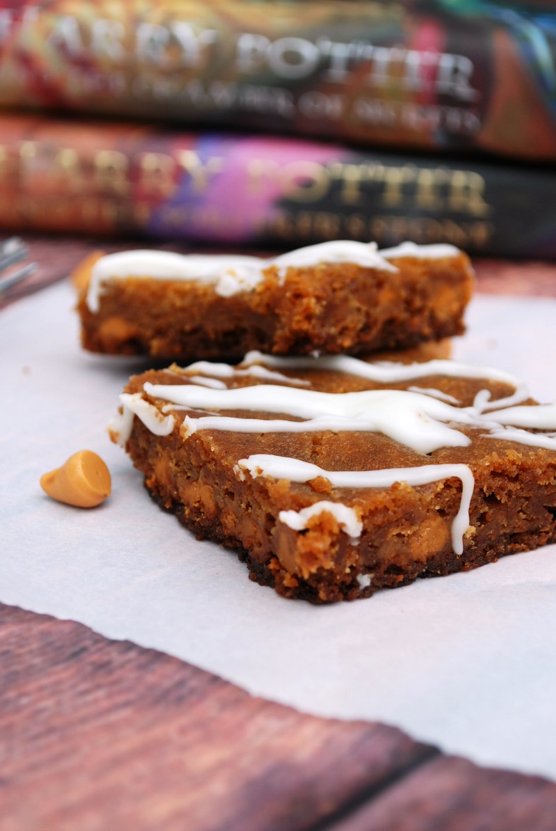 two butterbeer blondies with icing drizzle on napkin with harry potter book behind