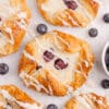 sourdough danish pastries spread on counter with blueberries around them and all drizzled with icing