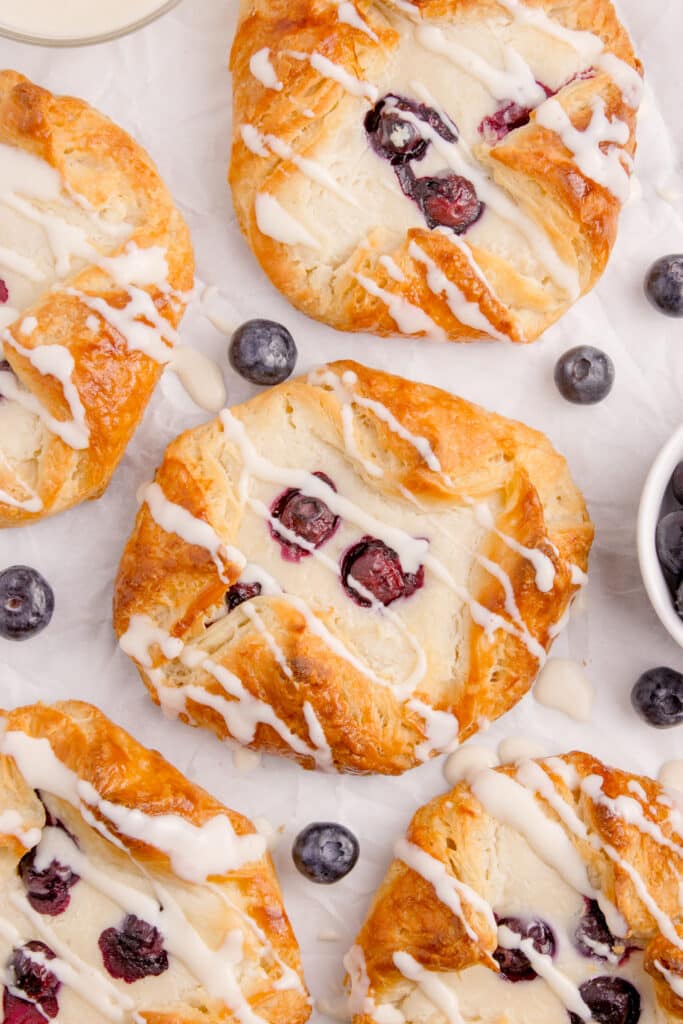 sourdough danish pastries spread on counter with blueberries around them and all drizzled with icing