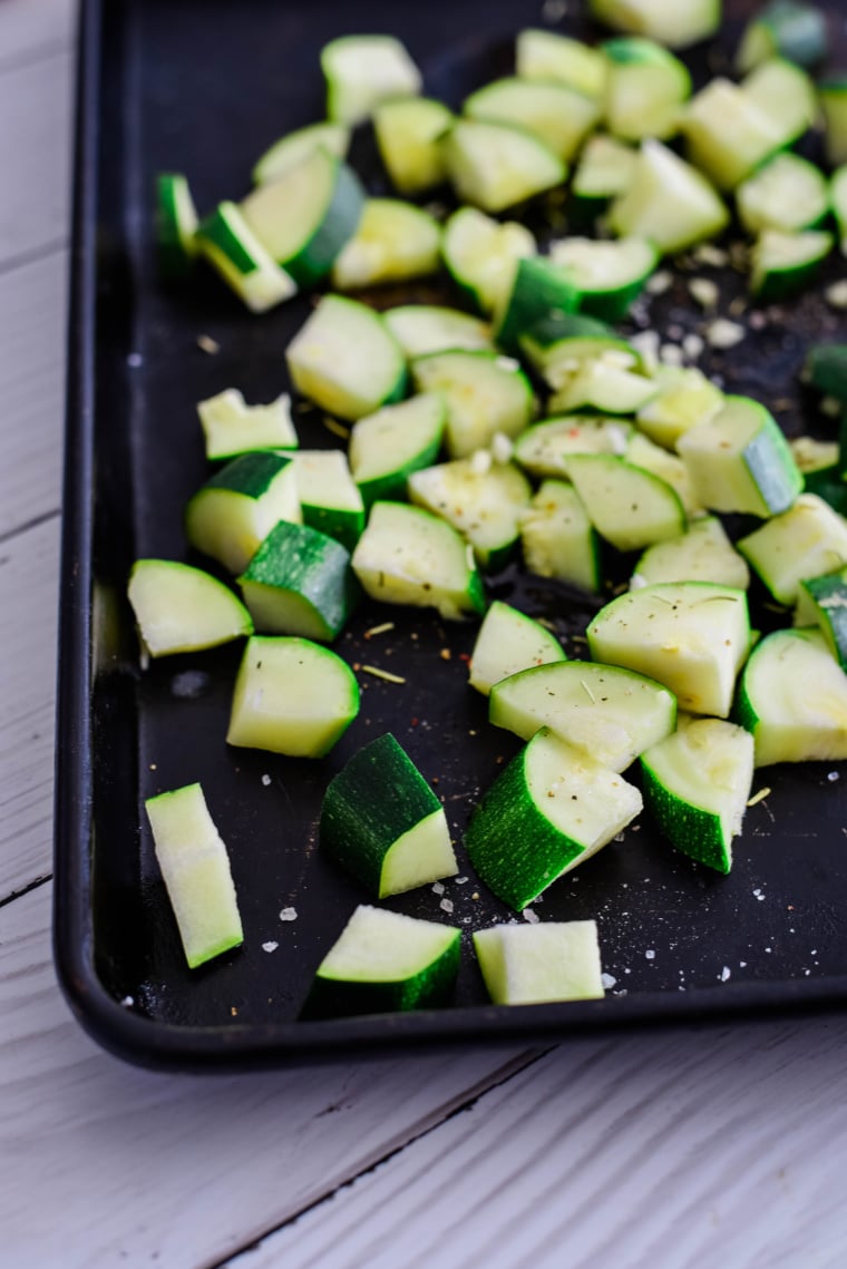 diced zucchini on roasting pan drizzled with olive oil and fresh rosemary