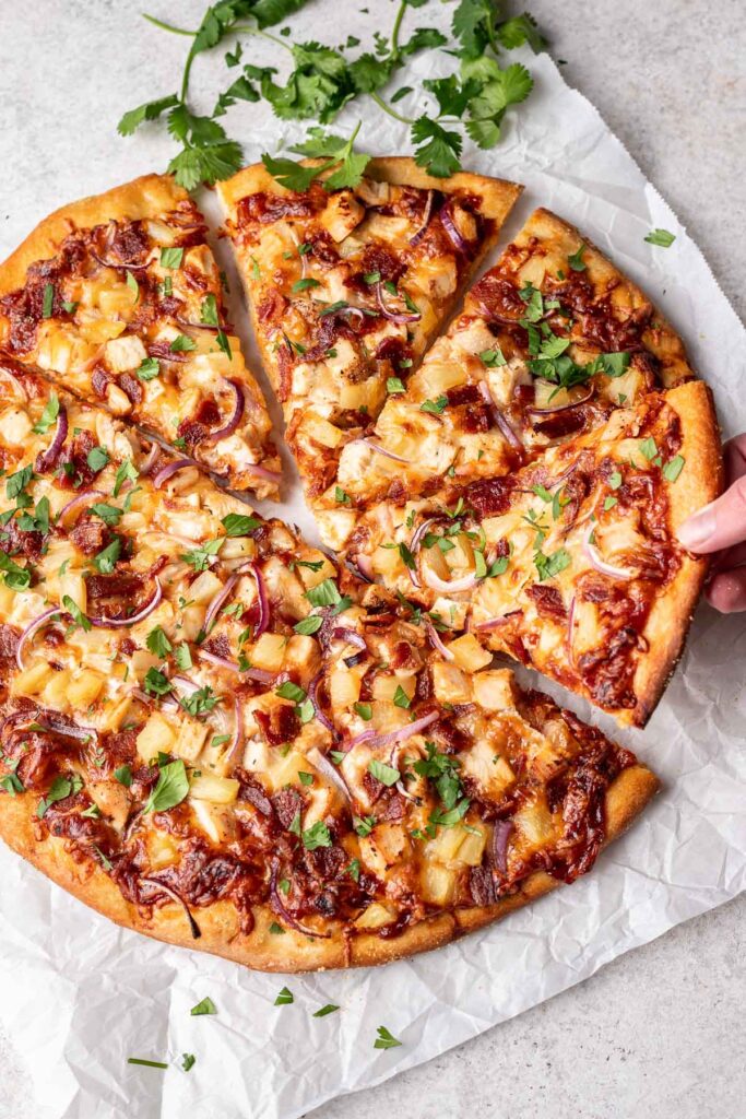 hawaiian bbq chicken pizza on counter with hand pulling out a slice