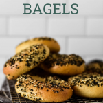 sourdough bagels piled on cooing rack with recipe title text overlay for pinterest