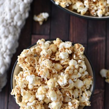 A bowl of peanut butter popcorn sitting on a wooden table next to a knitted blanket