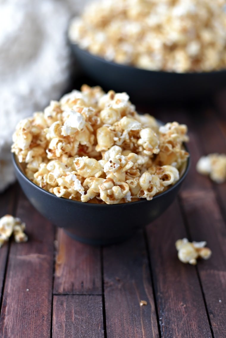 A black bowl with peanut butter popcorn sitting on a wooden table