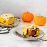 pumpkin cinnamon roll on plate with fork and pumpkins behind