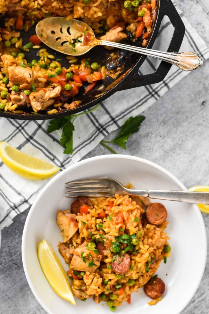 cast iron skillet with paella with filled plate with a lemon slice and a fork