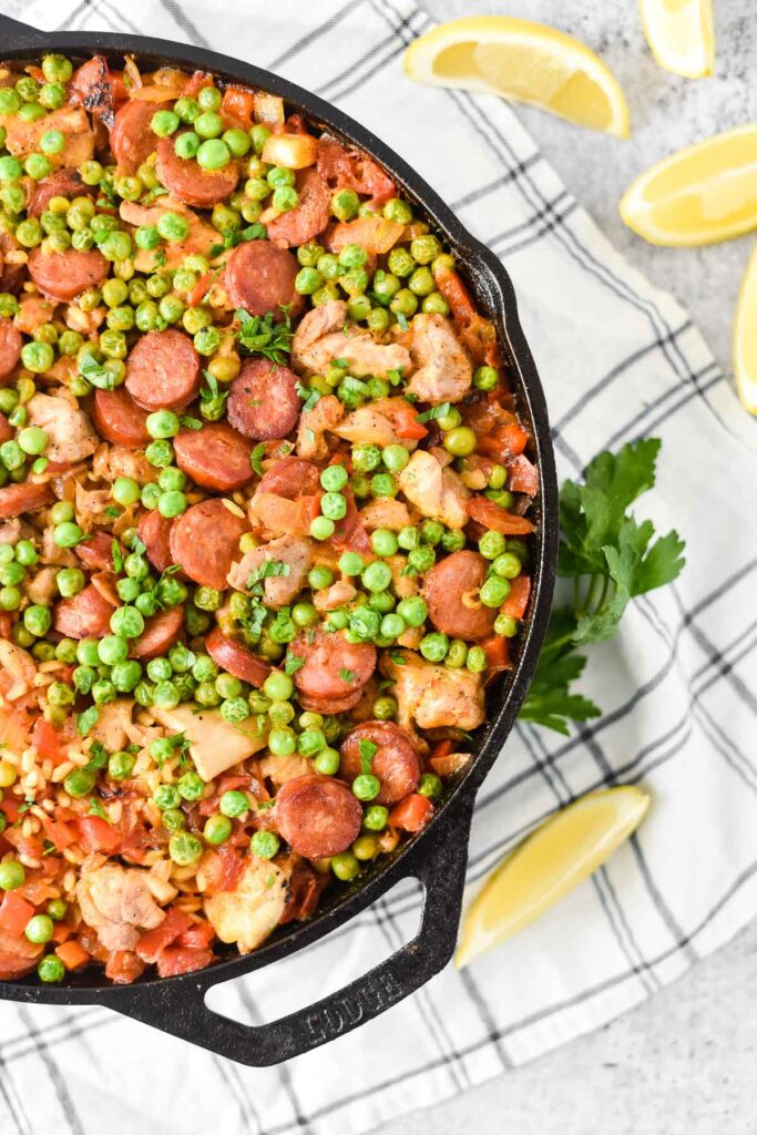 overhead view of cast iron skillet filled with paella with lemon slices and parsley around
