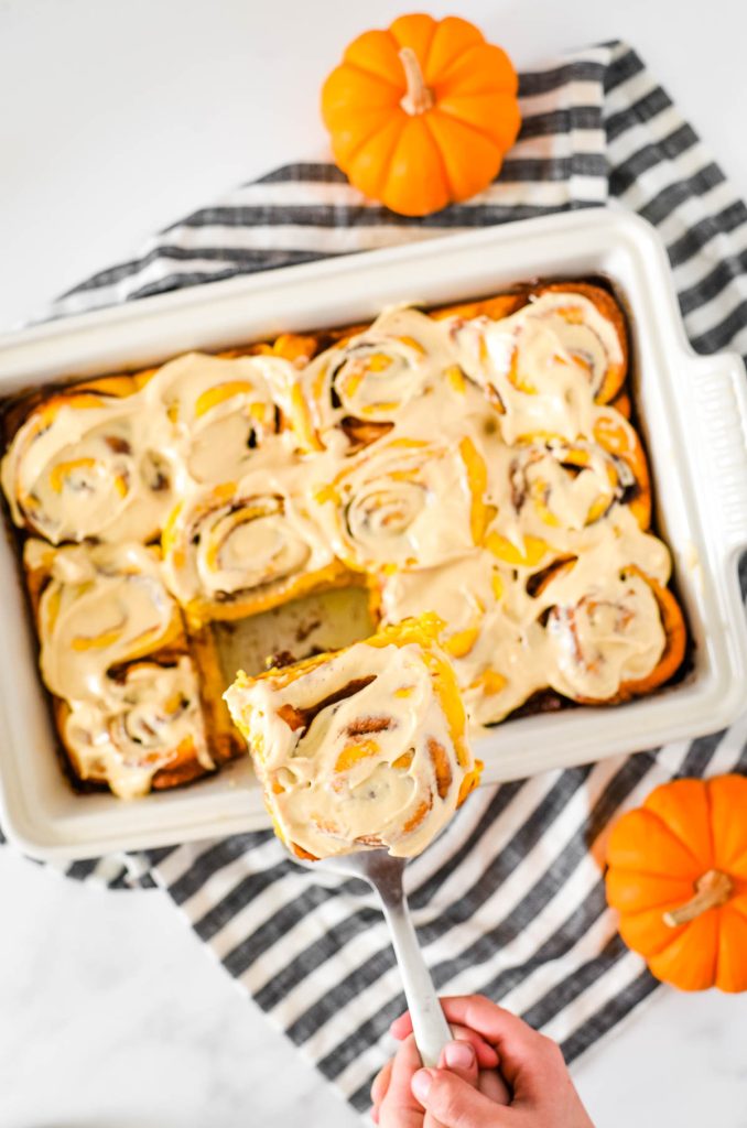 pumpkin cinnamon rolls in white dish with hand removing piece