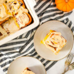 overhead view of pumpkin cinnamon rolls on plates with pumpkins and dish beside