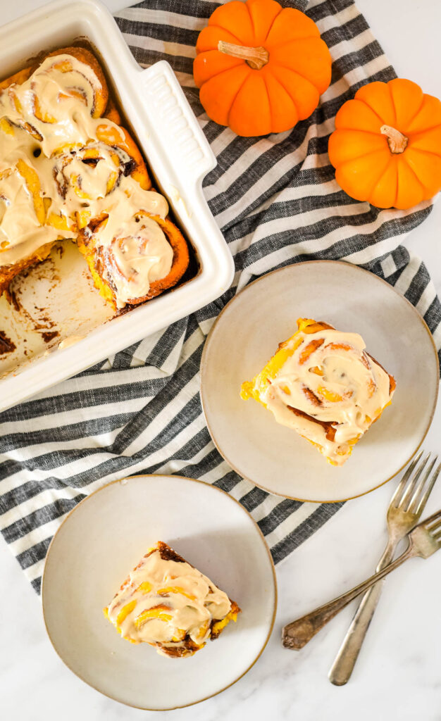 overhead view of pumpkin cinnamon rolls on plates with pumpkins and dish beside