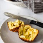 close up view of sourdough popover split open, on plate with buttered knife