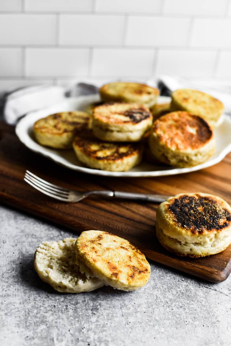 sourdough english muffins on white platter and wooden cutting board