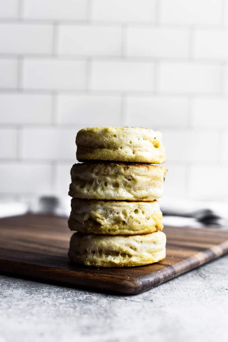 sourdough english muffins in a stack sitting on a wooden cutting board