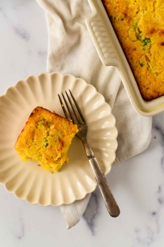 a slice of cornbread with jalapeños and cheese on a white plate with a fork next to baking dish
