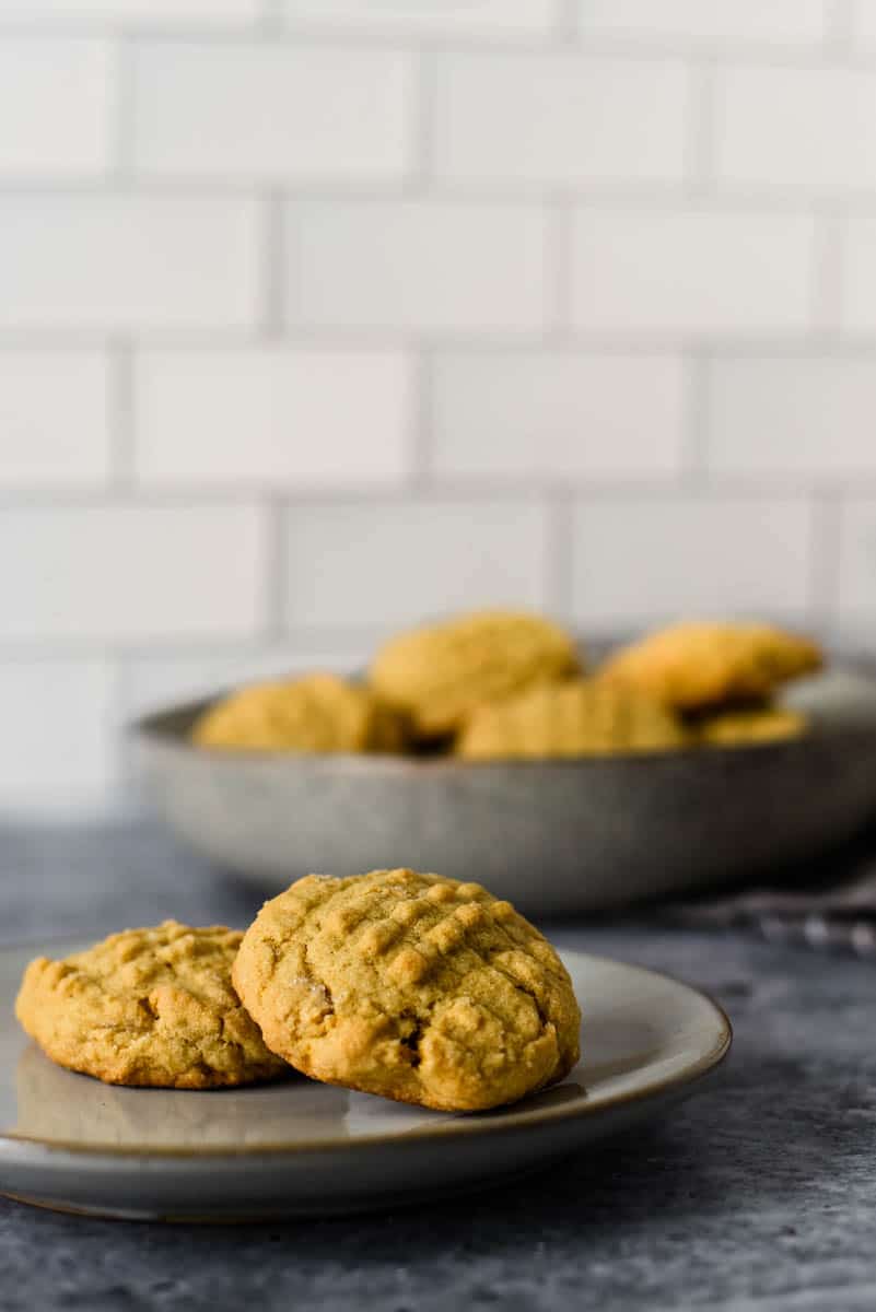 two peanut butter sourdough cookies on a plate in front of bowl full of cookies