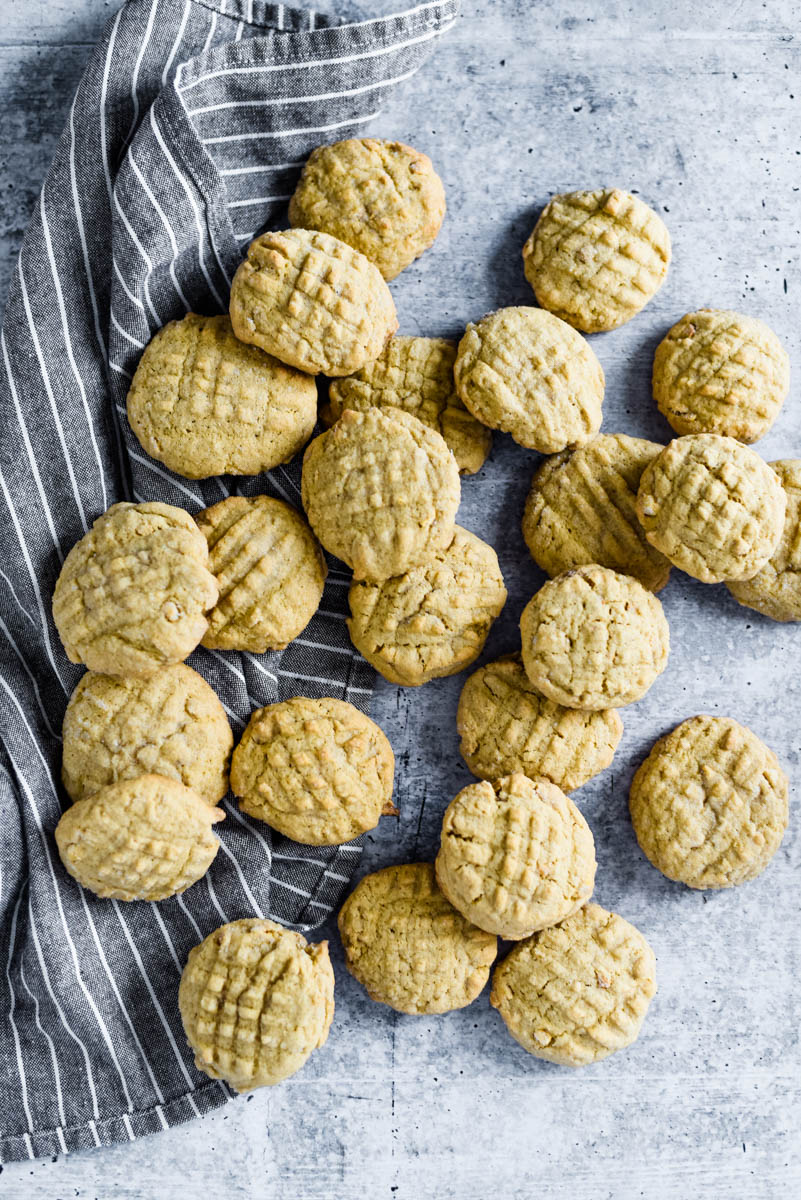 two dozen sourdough peanut butter cookies scattered on a grey striped tea towel