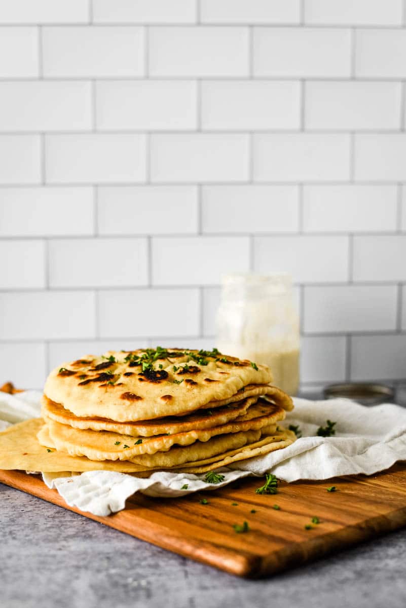 stack of eight sourdough naan beside glass jar with sourdough starter